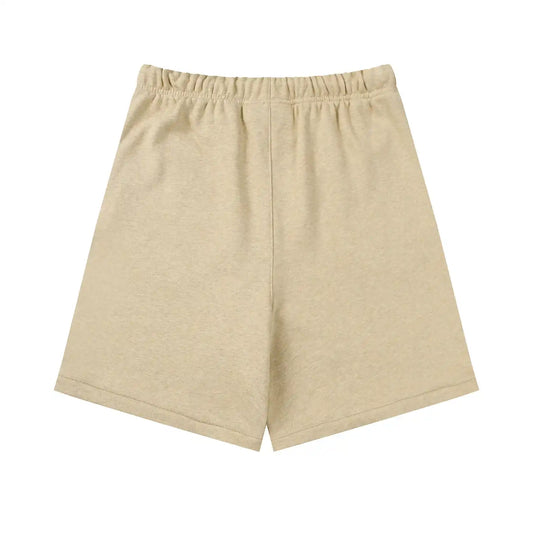 Fear of God Essentials Calm Shell beige shorts, front view, showing a relaxed fit with an elastic waistband and subtle “ESSENTIALS Fear of God” logo detailing