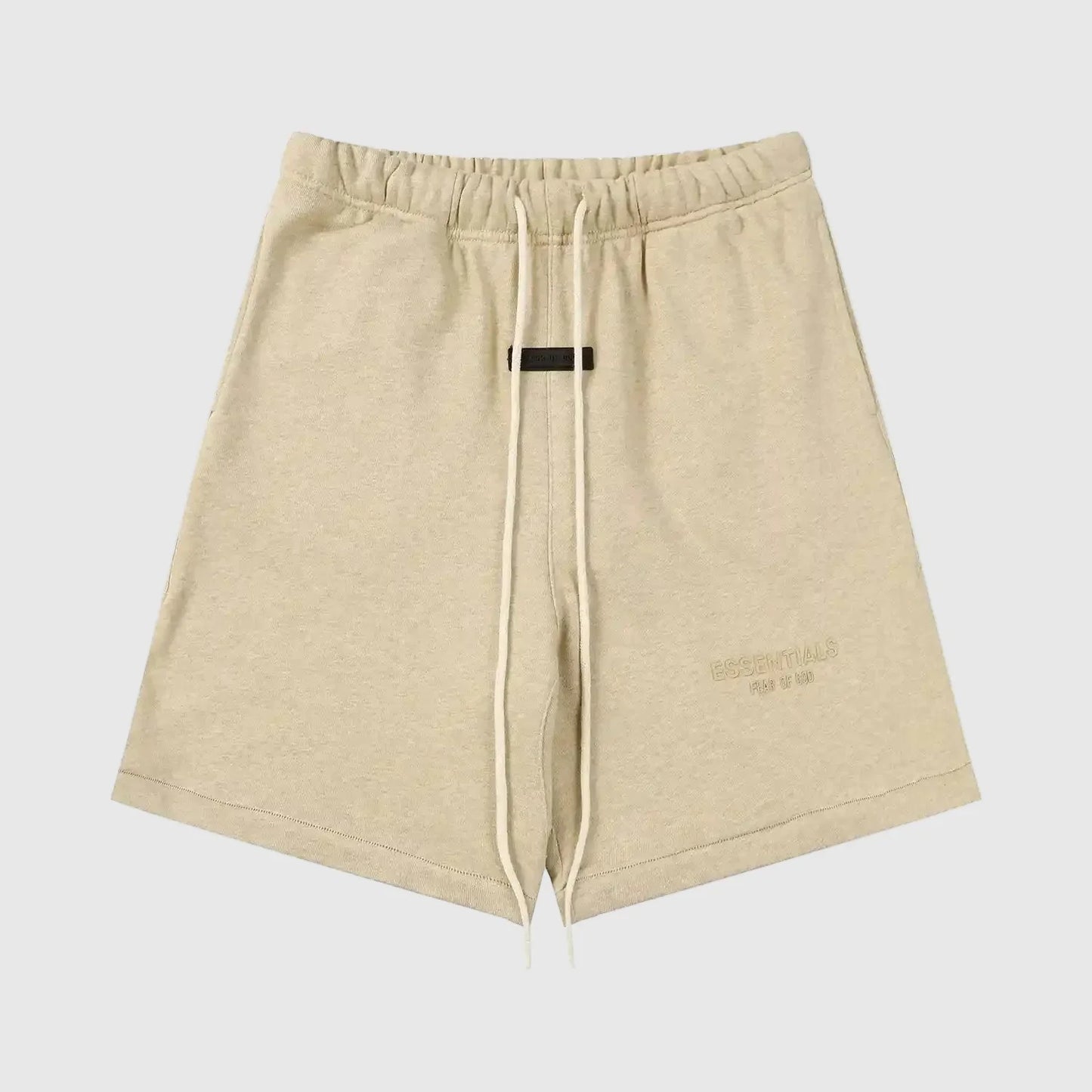 Fear of God Essentials Calm Shell beige shorts, front view, showing a relaxed fit with an elastic waistband and subtle “ESSENTIALS Fear of God” logo detailing