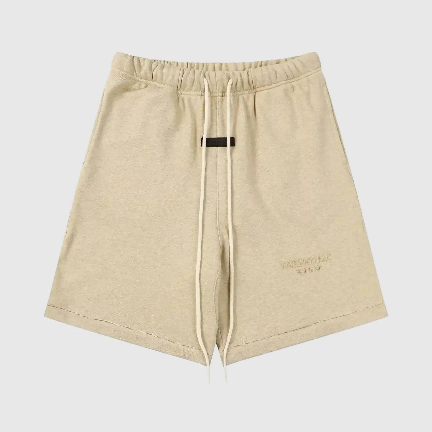 Fear of God Essentials Calm Shell beige shorts, front view, showing a relaxed fit with an elastic waistband and subtle “ESSENTIALS Fear of God” logo detailing