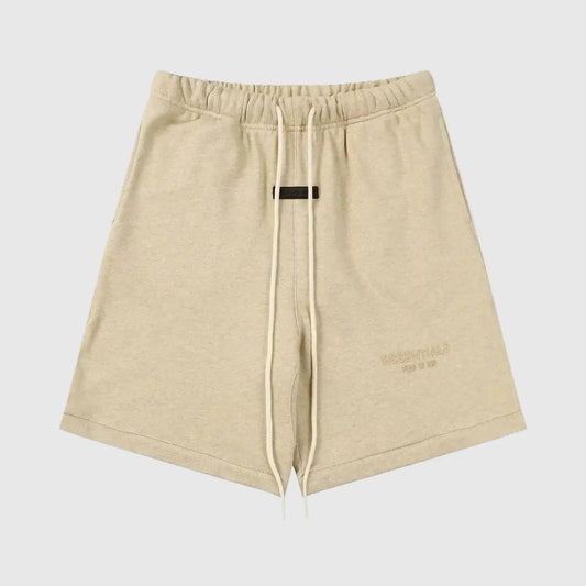 Fear of God Essentials Calm Shell beige shorts, front view, showing a relaxed fit with an elastic waistband and subtle “ESSENTIALS Fear of God” logo detailing